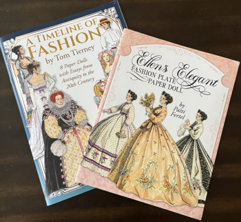  Two books lay on a wooden table they are A Timeline of Fashion by Tom Tierney and Ellen's Elegant Fashion Plate Paper Doll by Patti Fertel. 
